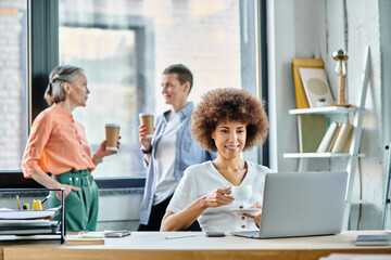 Hard working african american businesswoman using laptop, with her diverse colleagues on backdrop.