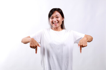 Portrait of young asian woman standing pointing fingers down and smiling, showing banner, click on...