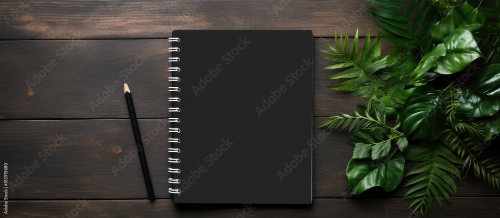 Poster top view of a notebook placed on a black wooden background with green leaves creating a visually app