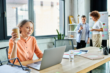 A woman fully engrossed in her work, sits before a laptop in a modern office space, with her...