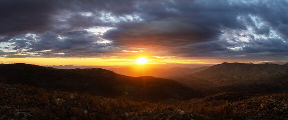 Panorama of a mountain landscape with a brilliant sunset between the land and the clouds.