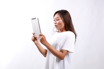 Portrait of young asian woman looking at digital tablet with surprised, shocked face, side view....