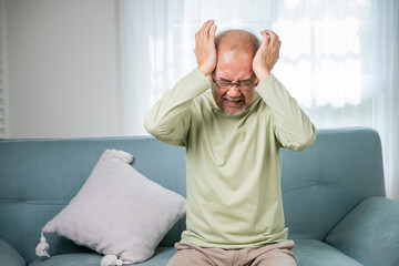 Headache. Sad Asian senior man sitting on sofa feeling hurt and lonely, elderly holds head with...