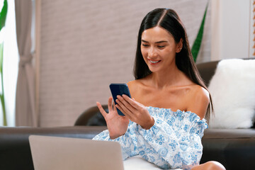 Young woman using laptop, happily browsing the internet or making online purchases on sofa at home....