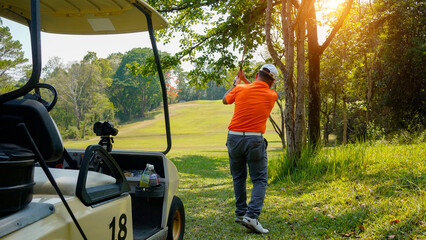 Golfer plays golf on the fairway with golf cart in the evening at sunset background.