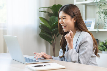 Happy cheerful asian young woman celebrate online looking at laptop computer screen, receive good news, enjoying with great offer from social, hands expression, gesture successful on desk at office.