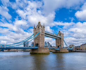 Obraz premium Panoramic view of London's Tower Bridge from the River Thames with maritime traffic and ferries sailing along the river under a blue sky with white clouds. United Kingdom.