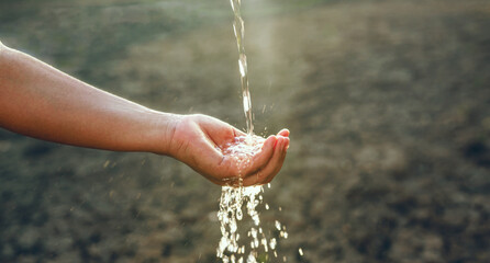 hand is holding a faucet and water is spraying out. The water is splashing and creating a misty...