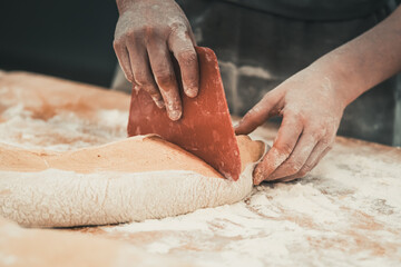 A female baker divides pieces of dough with a dough cutter