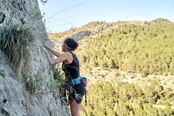 A woman is scaling a steep rock wall in the mountains, demonstrating her climbing skills and...