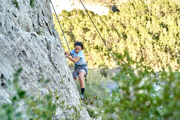 A boy determinedly scales a rocky mountain, clinging to the rough surface as she practices climbing...