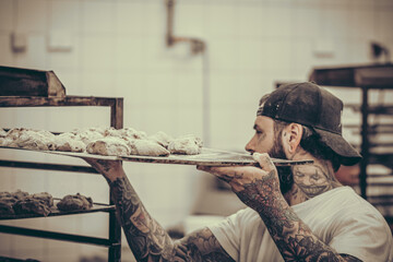 The baker pushes a tray of raw rolls of dough into a cart, vintage style with grain