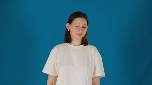 Confident woman points fingers at appearance on blue background. Selfish lady in white t-shirt performs proudness in studio. Self esteem