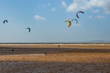 Kite surfers in the waves on a windy day. Bright colourful kites fill the sky. contrasting shadows are cast on the water. copy space.