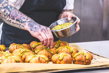 Confectioner's hand with tattoos decorating tartlets with pistachios. Preparation of the tartlets by a professional pastry chef.