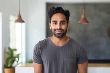 Fototapeta premium Portrait of a satisfied indian man in his 20s smiling at the camera in front of modern minimalist interior