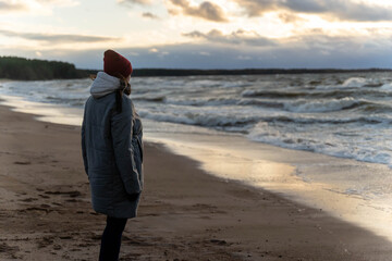 a woman stands on the seashore in the cold during a storm. 