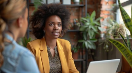 A psychologist conversing online with a client, shown on a laptop screen in a modern, plant-adorned office.