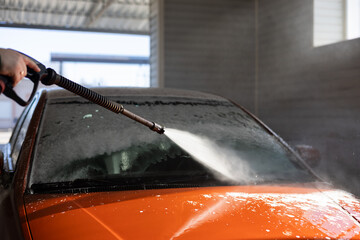 Using a water pistol, the driver washes off foam and remaining dirt from the windshield of the car....