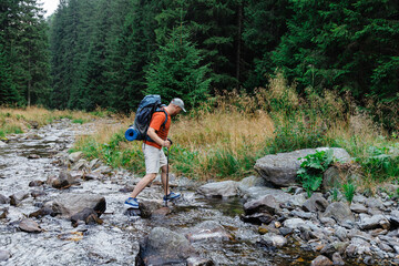 Male hiker crossing creek in forest