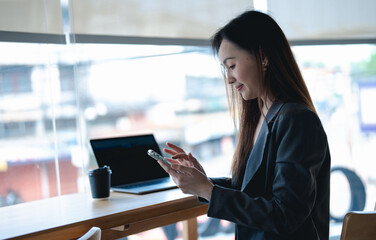 Fototapeta premium Asian young beautiful happy professional successful businesswoman designer sitting smiling at workstation desk using laptop notebook computer and smartphone working remotely online at home office