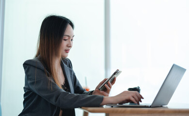 Asian young beautiful happy professional successful businesswoman designer sitting smiling at workstation desk using laptop notebook computer and smartphone working remotely online at home office
