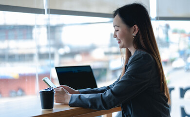 Asian young beautiful happy professional successful businesswoman designer sitting smiling at workstation desk using laptop notebook computer and smartphone working remotely online at home office