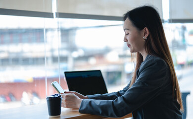 Fototapeta premium Asian young beautiful happy professional successful businesswoman designer sitting smiling at workstation desk using laptop notebook computer and smartphone working remotely online at home office
