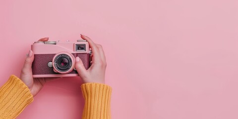 Holding a pink retro camera in hands on a pink background.
