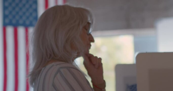 Mature woman voting at a polling station with another female voter in the background.