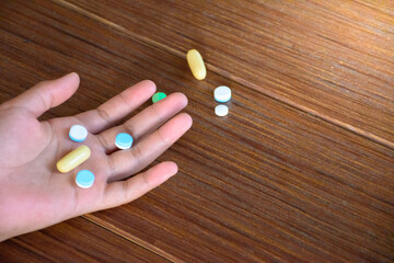 Hand and many colorful pills on wood pattern floor top-view for concept of overdose and medicine.