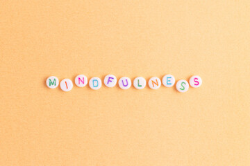 Mindfulness. Word made of white round beads with multicolored letters on a gold colored background.