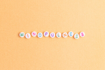 Mindfulness. Word made of white round beads with multicolored letters on a gold colored background.