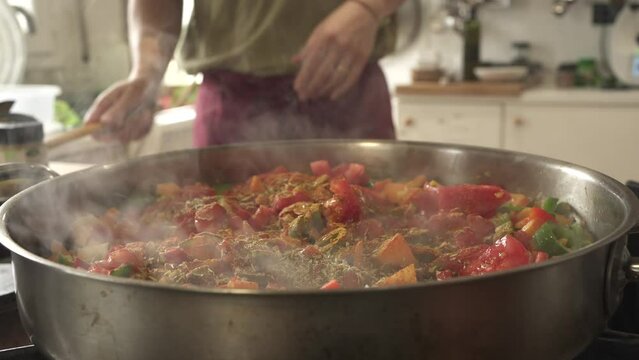 unrecognisable man putting spices in sofrito in large paella, cooking for many people
