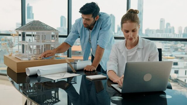 Smart architect engineer inspect house model while colleague using laptop analysis data. Professional designer team working together to design house model construction at modern office. Tracery