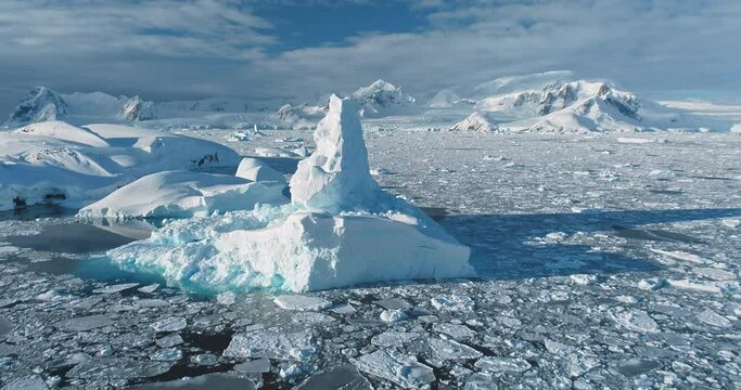 Aerial view panorama massive iceberg floating frozen ocean in Antarctica. Majestic winter Antarctic glacier melting under sun. Snow covered mountains blue cloudy sky. Global warming and climate change