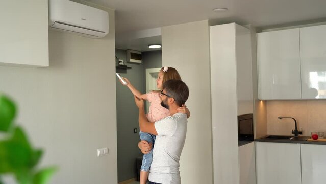 Father with little child turn on air conditioner using remote control. Happy family adjust comfortable temperature of cooler system in apartment
