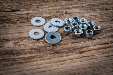 Stack of flat washer and zinc plated hexagon nuts on a dark wood texture background