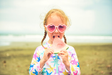 Portrait of girl of 4 years with heart-shaped sunglasses on beach of Costa Rica eating watermelon