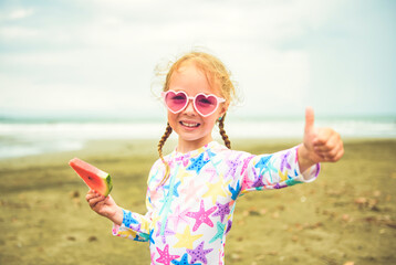 Portrait of girl of 4 years with heart-shaped sunglasses on beach of Costa Rica eating watermelon