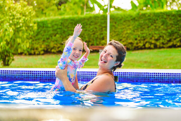 mother with little girl in pool on sunny day.