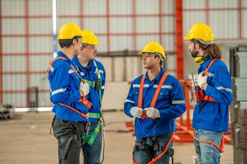 Four construction workers wearing yellow hard hats and blue coveralls are having a discussion at a construction site.