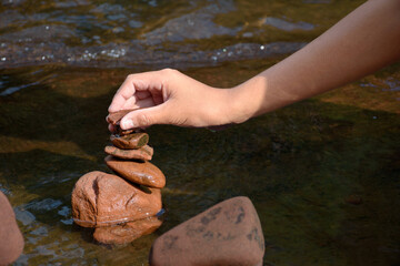 Hand holding stone for balancing stone and zen stacked rock on river flowing background.
