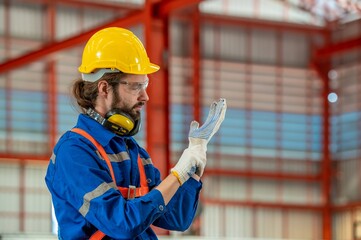 A man wearing a hard hat and safety glasses puts on his gloves.