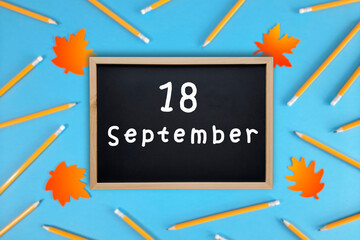 September 18 written in chalk on black board. Calendar date 18th of September on chalkboard on blue blurred school stationery background. Back to school. School event schedule date. Month of autumn.