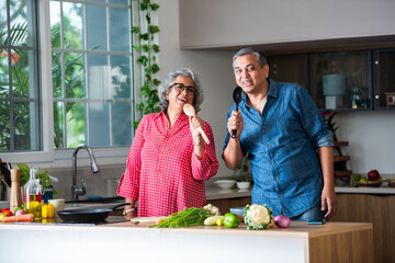 Indian asian retired old senior couple singing in kitchen while cooking food