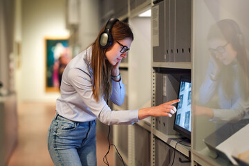 Woman wearing headphones and contemplates ancient arts. Student visiting gallery or museum. Concept...