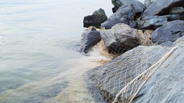 An abandoned fishing net on the shore of the lake. Poaching of fish. The concept of nature conservation.