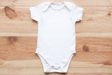 Mockup of white baby bodysuit on wood background. Blank baby clothes template, flat lay.