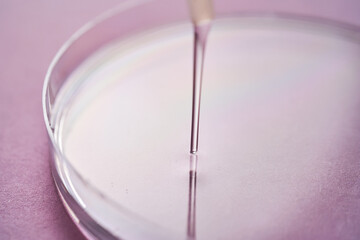 Serum or cosmetic oil flows into a transparent bowl on a purple background.